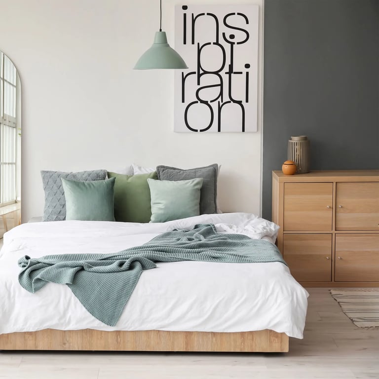 Bett mitten im Raum stehend, mit mintfarbener Tagesdecke. Im Hintergrund ein Bild auf dem Inspiration steht.