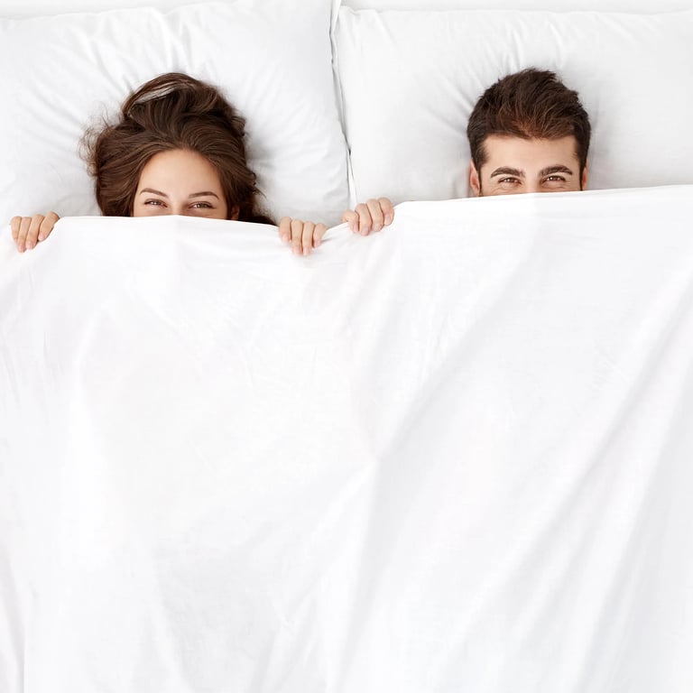 Pärchen hält dich die Bettdecke halb über das Gesicht