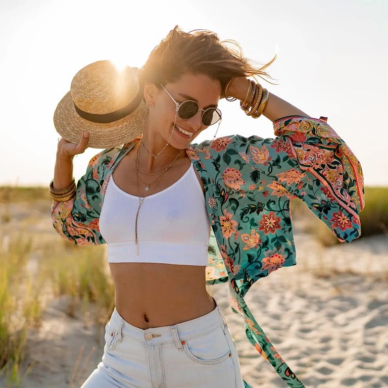 Frau mit Sonnebrille und Strohhut freudig am Strand
