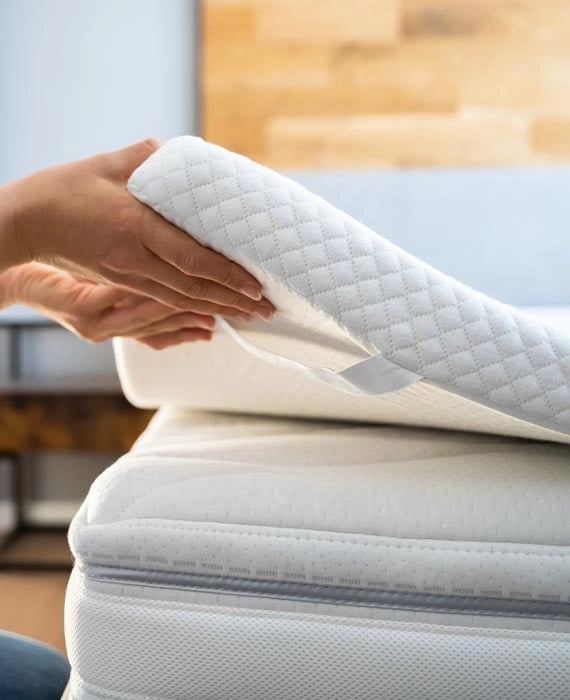 Eine Hand hält einen Topper von der Matratze hoch