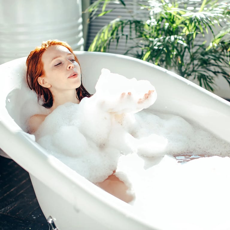 Frau in Badewanne mit Schaum in der Hand, den sie wegbläst