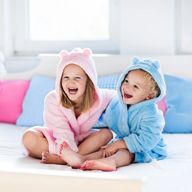 Junge und Mädchen sitzend mit Bademänteln in blau und pink