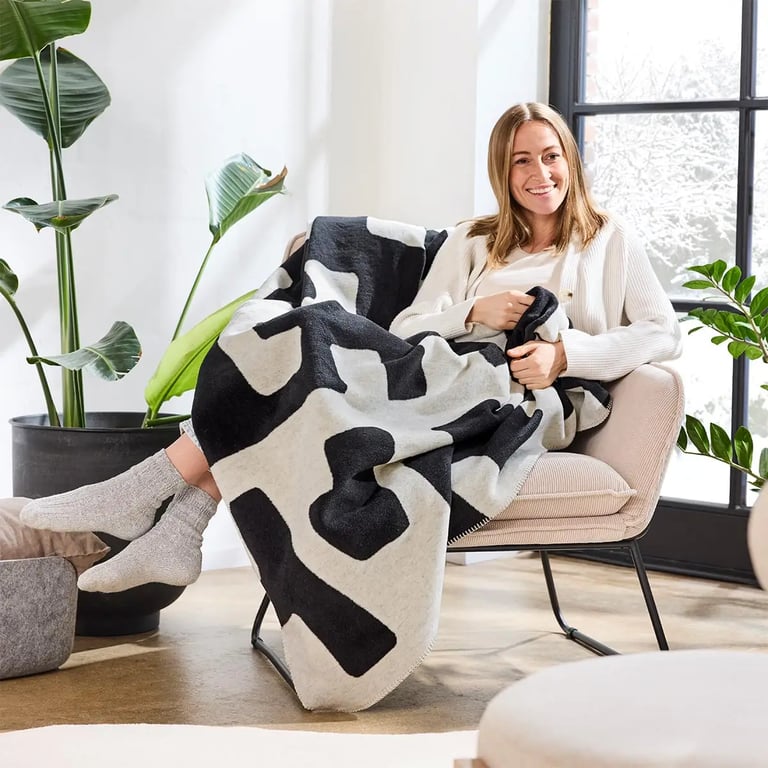 Dame auf einem Stuhl sitzend eingehüllt in eine schwarz weiße Ibena Wohndecke