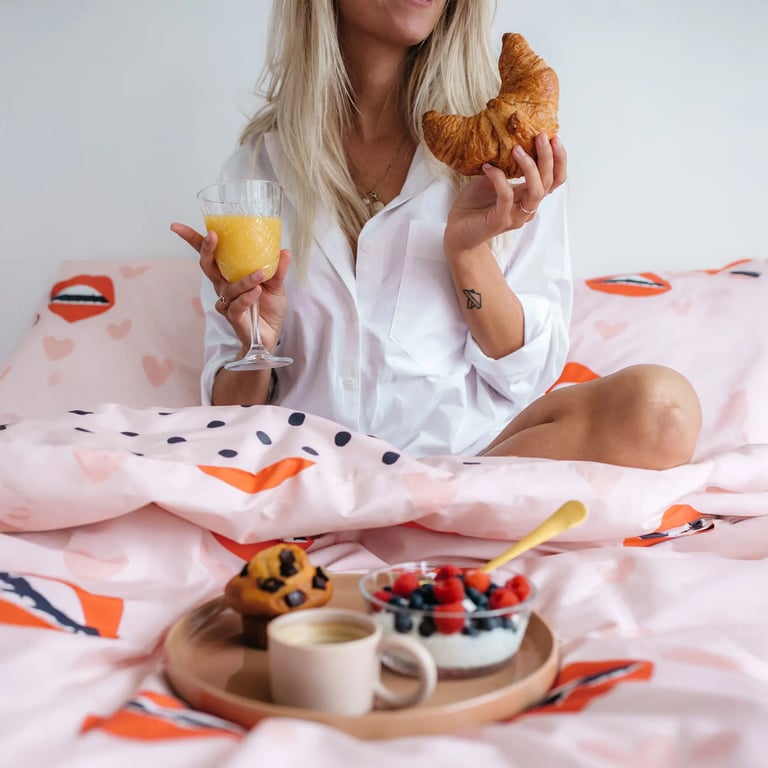 Frau frühstückt im Bett mit Croissant und Orangensaft