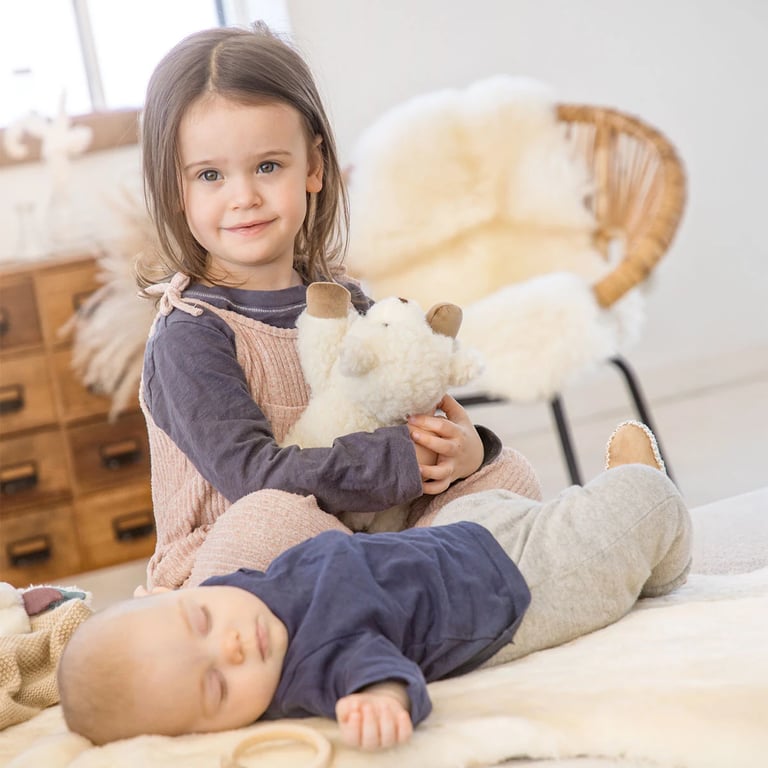 Ein Kleinkind hält ein Kuscheltier in den Armen, vor ihm liegt ein Baby